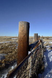 Wooden posts on field against clear sky during winter