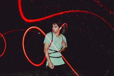 Young man standing around red light trail in dark at night