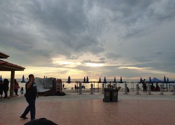 People walking on beach against sky during sunset