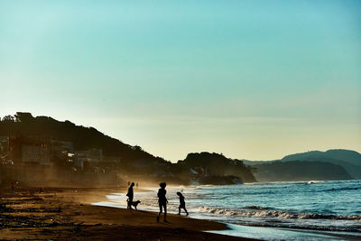 Silhouette people on beach against sky during sunset