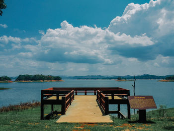 Empty bench by lake against sky