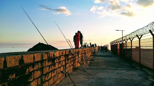 People fishing by sea against sky during sunset