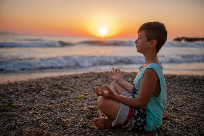 Boy meditating at beach during sunset