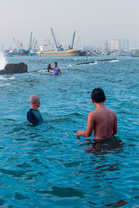 Rear view of shirtless men in sea against sky