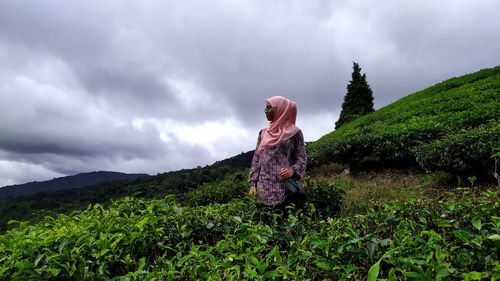 Woman standing by plants on land against sky