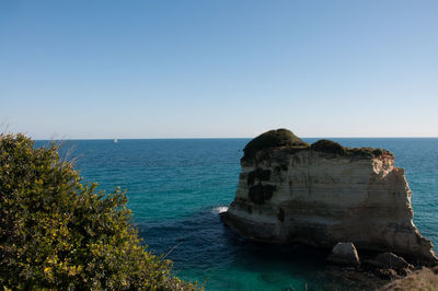 Rock formations by sea against clear blue sky