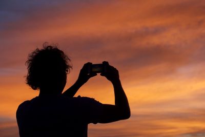 Silhouette man photographing with camera against sky during sunset