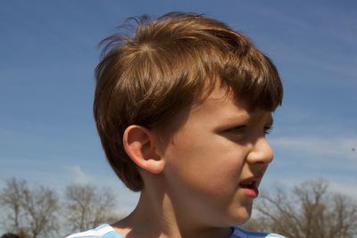 Close-up of boy looking away against sky during sunny day