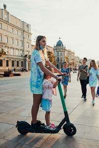 Teenager girl and her sister preschooler riding an electric scooter in the city center