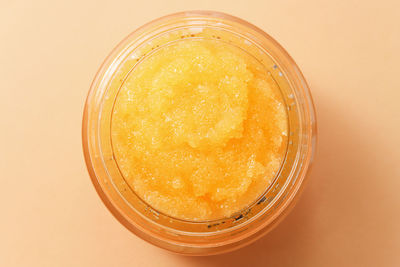 Close-up of a glass container with an orange-colored sugar body scrub, top view.