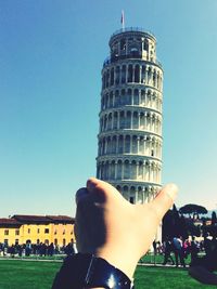 Optical illusion of hand holding leaning tower of pisa against sky