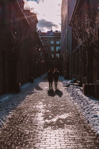 Rear view of people walking on footpath amidst buildings in city