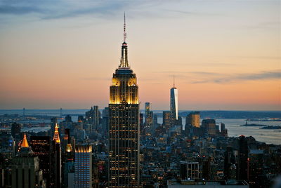 Illuminated empire state building and cityscape against sky during sunset