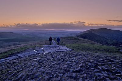 People on land against sky during sunset