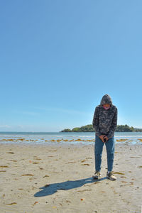 Rear view of woman standing at beach against clear sky