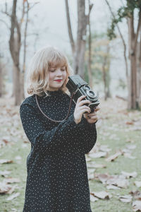 Young woman photographing from camera while standing on field