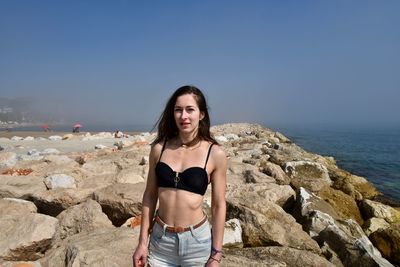 Portrait of young woman standing on beach against clear sky