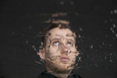 Reflection of young man on mirror with water against black background