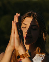 Close up portrait young woman practicing yoga and meditation with folded hands outdoors at sunset	

