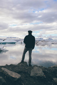 Full length rear view of man standing by lake against cloudy sky