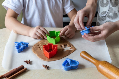 Mom and daughter with cookie cutters make christmas cookies from dough in the home kitchen.