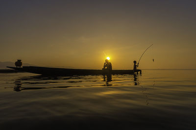 Silhouette people fishing in sea against sky during sunset