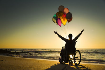 Rear view of man with balloons at beach during sunset