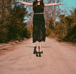 Cropped image of woman in black dress jumping with arms outstretched