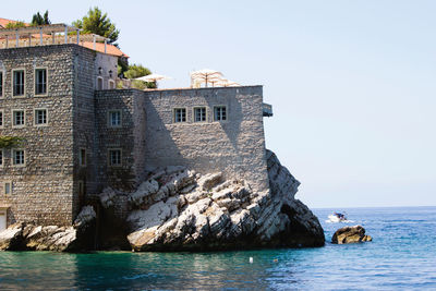 Built structure on rocks by sea against clear sky