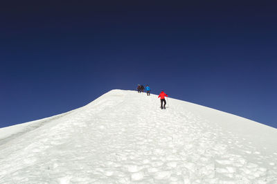 Low angle view of people walking on snowy landscape against clear blue sky