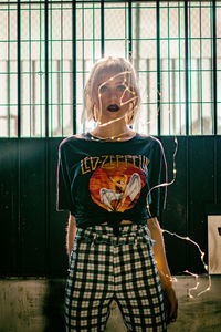 Portrait of woman holding camera while standing against window