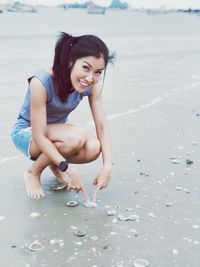 Portrait of smiling mid adult woman pointing fingers towards seashell at beach