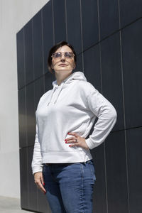 Closeup pretty mature brunette woman in white hoody, jeans and sunglasses looks away on dark