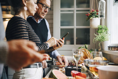 Senior woman showing smart phone to man while preparing dinner in kitchen