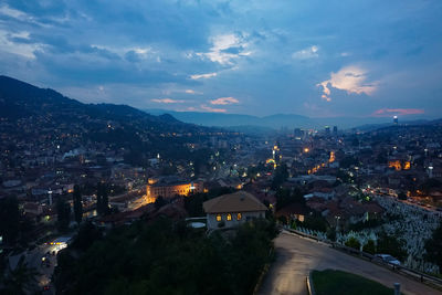 High angle view of illuminated cityscape against cloudy sky during sunset