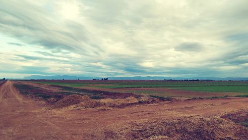 Road passing through field against cloudy sky