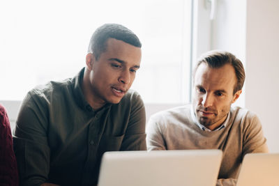 Confident multi-ethnic male coworkers discussing over laptop at creative office