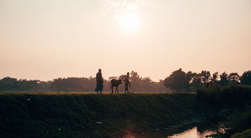 People returning home by walking on field against sky during sunset