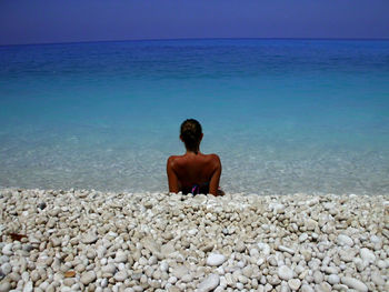 Rear view of woman sitting on rock at seaside