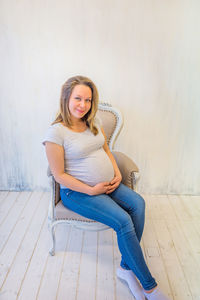 Pregnant woman sitting on chair against wall