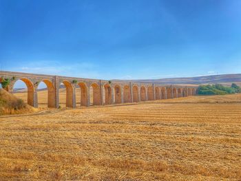 Arch bridge on field against sky