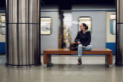 Full length of a young woman sitting on seat in the subway