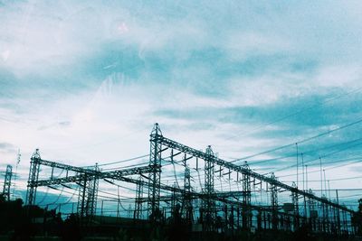 Low angle view of electricity pylon against cloudy sky