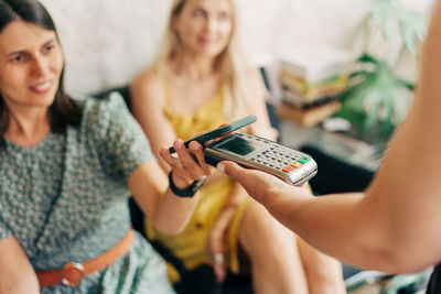 Women in a cafe pay contactlessly using their mobile phones.