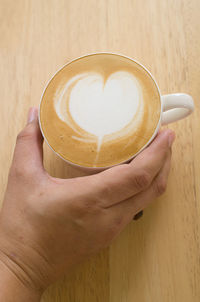 Close-up of hand holding coffee cup on table