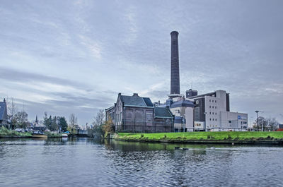 Buildings by river against sky