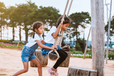 Side view of girl pushing sister on swing at playground