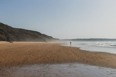 Distant view of man standing at beach against clear sky