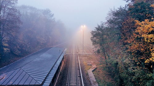 Railroad track amidst trees against foggy sky during autumn