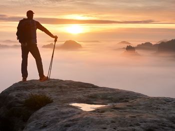 Man silhouette with poles in hand. sunny spring daybreak and  guide stay on  cliff of mountain